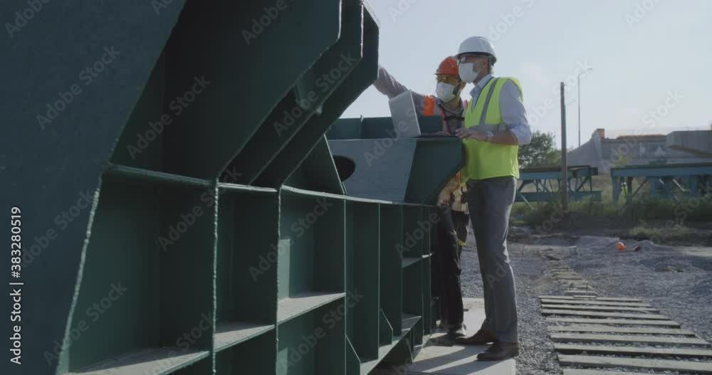 Engineers in masks using laptop on construction site Engineers in masks using laptop on construction site