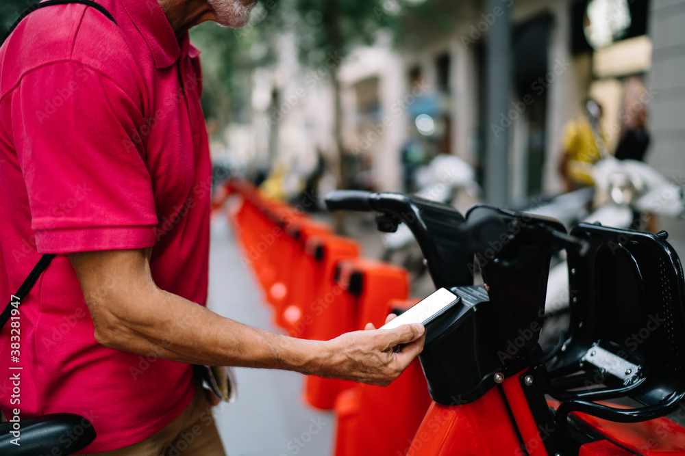Obraz premium Side view of cropped male tourist in pink shirt using contact payment for bicycle rent at city station for driving and have sightseeing, man with modern cellphone gadget connecting to application