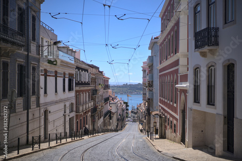 Fototapeta Naklejka Na Ścianę i Meble -  The light rails of route 28 Lisbon tramway, rua de Santo Domingos, Lapa (Portugal). The picture is shot in early morning, nobody can be seen. The river Tagus can be seen in the back. 