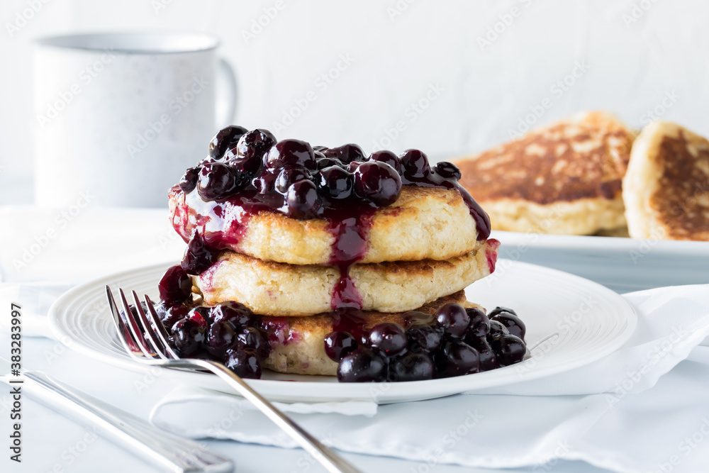 Stack of fluffy pancakes topped with warm blueberry sauce against a sunny window. Stack of fluffy pancakes topped with warm blueberry sauce against a sunny window.