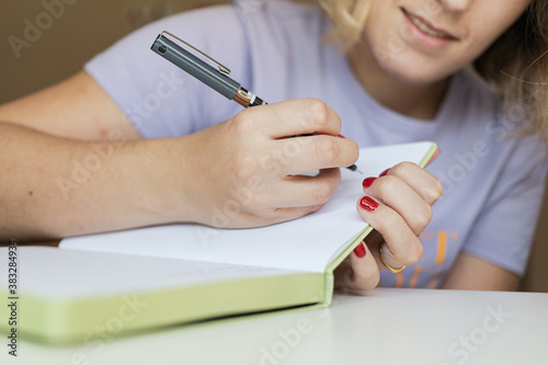 Blonde woman writing on her green notebook. Work from home concept