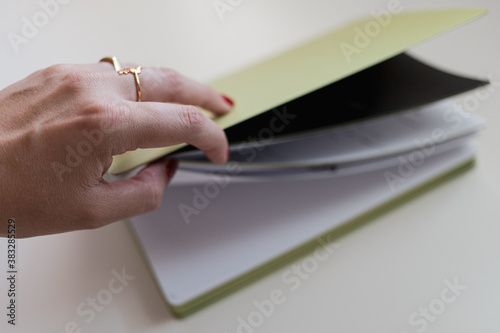 Woman hand with red nails and gold rings opening a green notebook