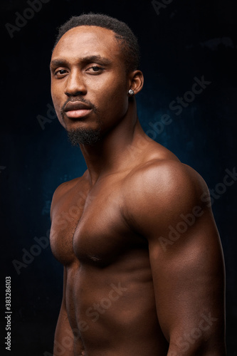 dark-skinned handsome man with a naked sports torso.on a dark background, he looks at the camera