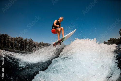 view of athletic man on surf style wakeboard jumping over splashing wave