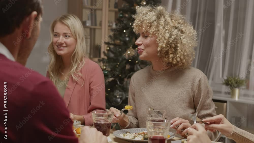 Back view of few multiethnic young people sitting at dining table, having Christmas celebration and eating tasty homemade food Back view of few multiethnic young people sitting at dining table, having Christmas celebration and eating tasty homemade food