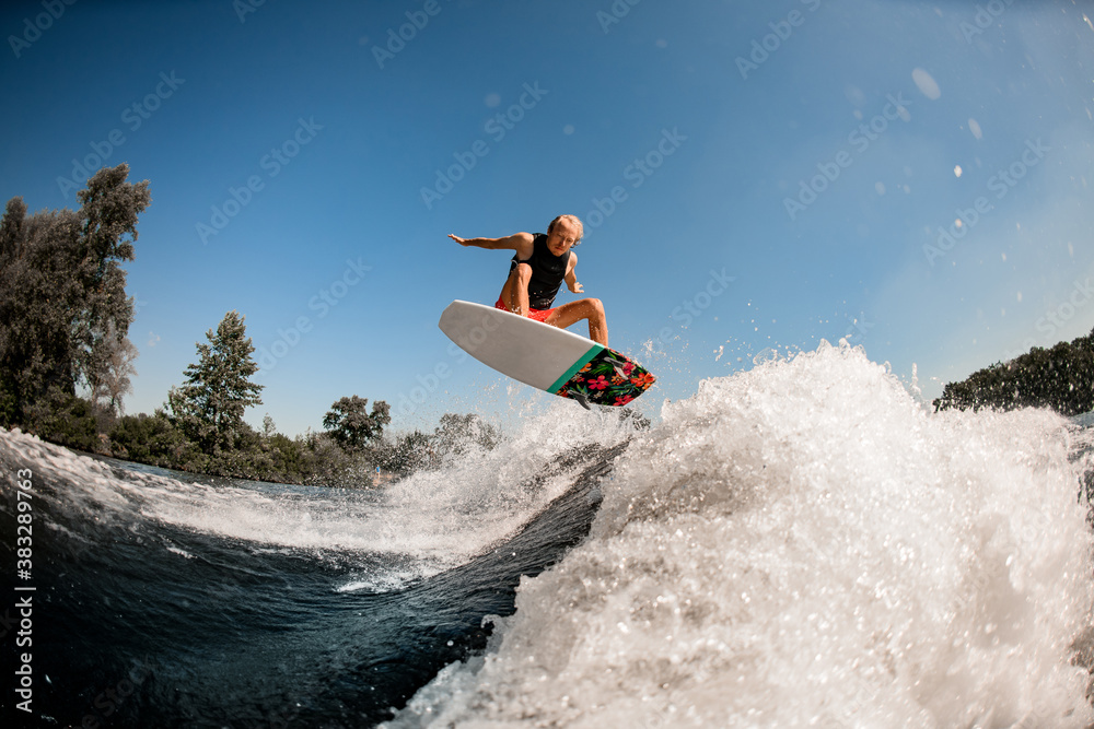 active energetic man on surf style wakeboard masterfully jumping over splashing wave