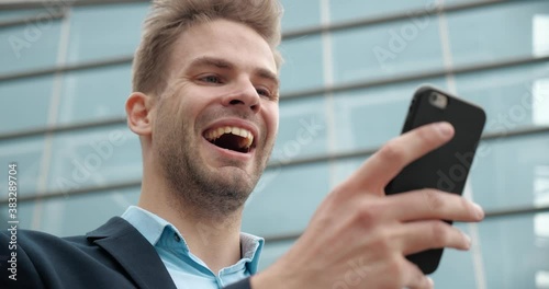 Close Up Portrait of Handsome Confident Caucasian Businessman is using browsing his Phone. Young Male is texting Messages, getting Positive Emotions while it. Smartphones. Business. People. photo