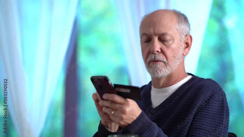 Closeup of mature man using credit card to make purchase on smartphone online, typing in account number, with glass of wine. Closeup of mature man using credit card to make purchase on smartphone online, typing in account number, with glass of wine.