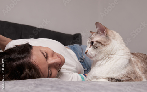 Woman lying on the bed with her white striped cat in a cute pose looking at each other