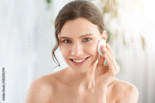 Canvas Print Smiling pretty young woman cleaning her face with toner