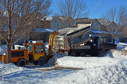 city snow removal equipment removing excessive snow from a neighborhood road, snow thrower discharges snow directly into a truck 