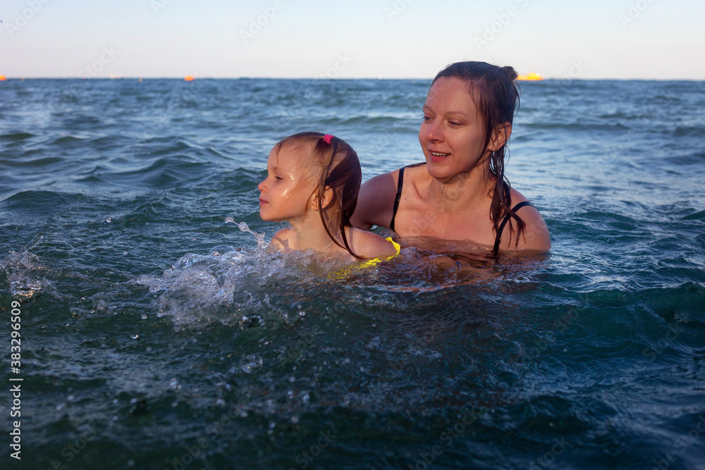 Mother is holding her little daughter. They bathe in the sea, many drops and spray adorable laughing having fun together hot summer day Mother is holding her little daughter. They bathe in the sea, many drops and spray adorable laughing having fun together hot summer day