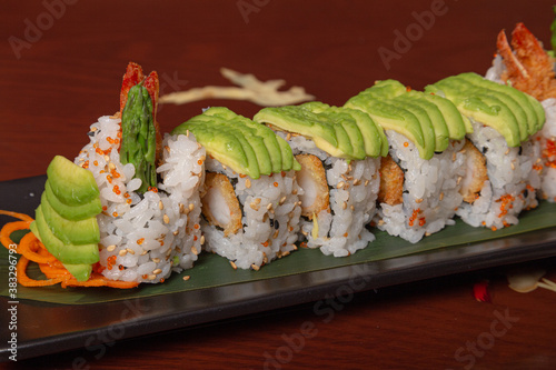 Grilled salmon sushi wrapped with avocado, prawn tempura and cheese on wooden table. Isolated image