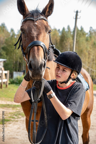 A girl in a black helmet leads a Bay horse on a warm early autumn day. © FO_DE