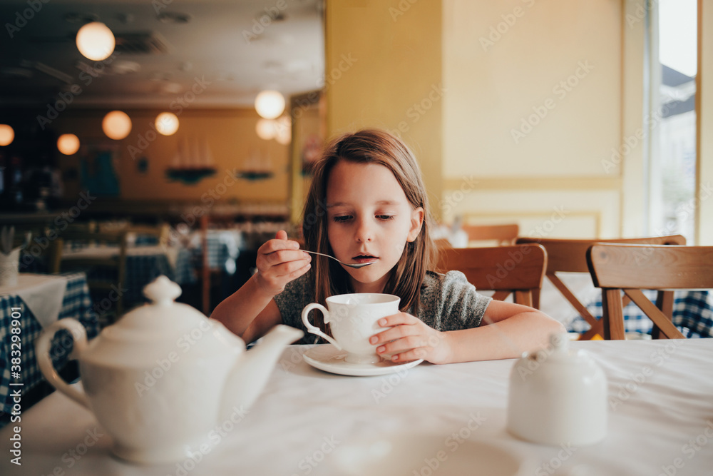 A little girl drinks tea in an empty cafe