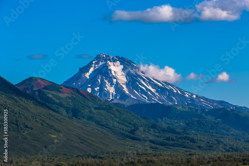 View of a mountain valley with a volcano in the background. There is snow on top of the volcano