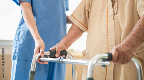 Close up of elderly patient hands using walking frame with nurse assistance. Medical professional or caregiver assisting senior man to walk with walker during recovery in hospital. 