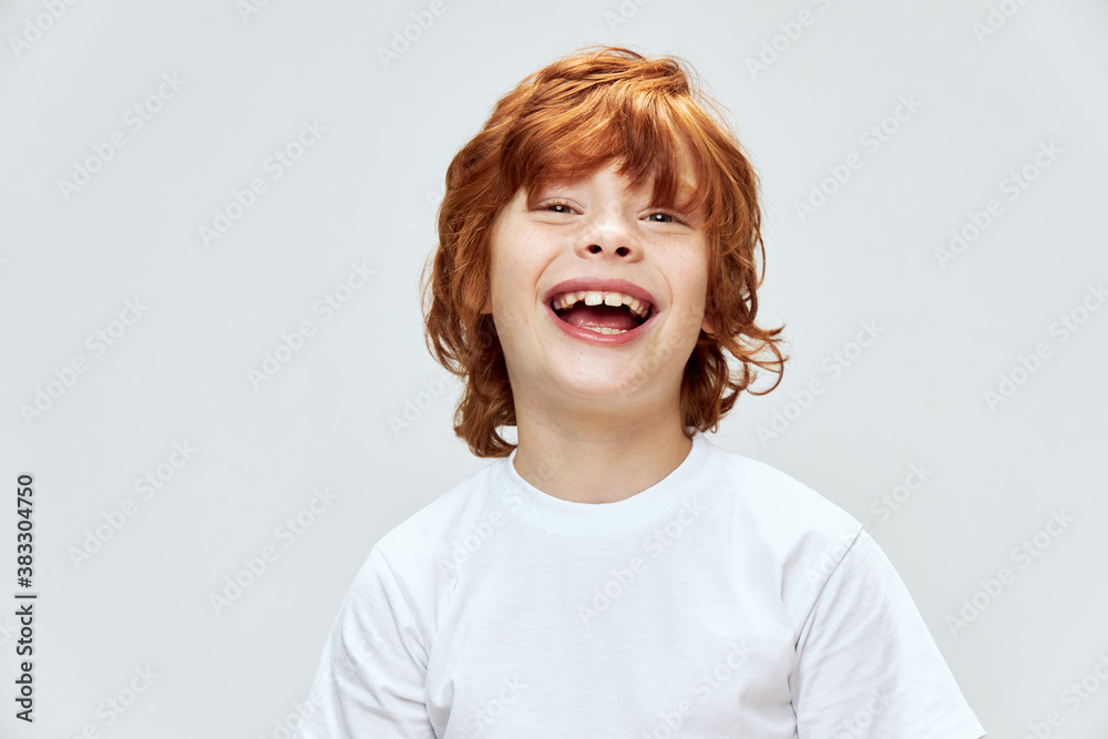 red-haired child with wide open smile in white t-shirt gray background 