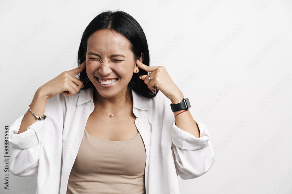 Photo of happy asian woman smiling and plugging her ears Photo of happy asian woman smiling and plugging her ears