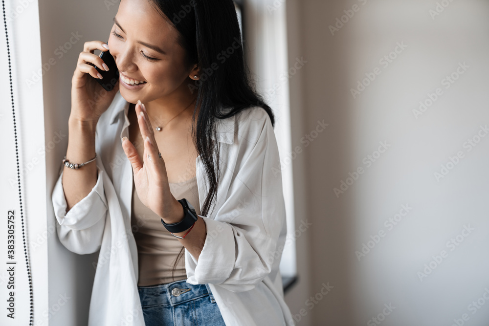 Photo of happy asian waving hand while talking on mobile phone Photo of happy asian waving hand while talking on mobile phone