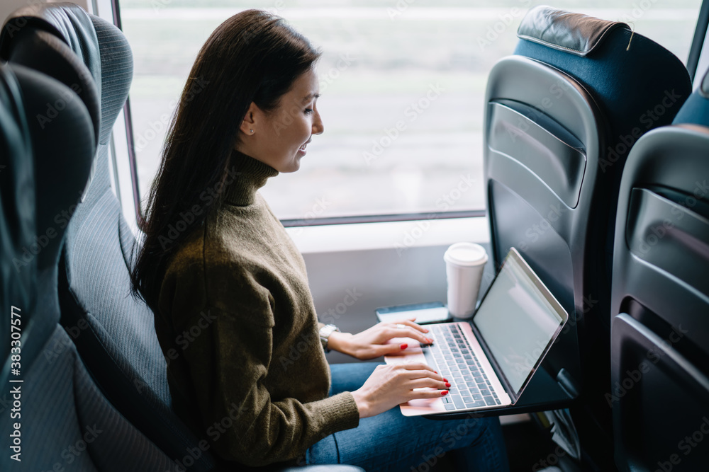 Cheerful asian female digital nomad working via technology and wireless connection during trip in wagon, smiling woman having distance job in train typing on laptop computer reading news on web page