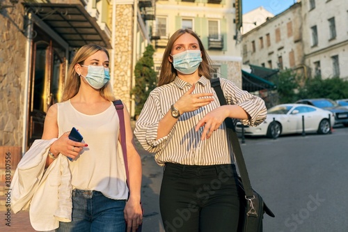 Two young business women in protective medical masks walking together