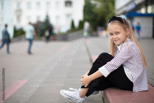 Beautiful little girl in an urban setting. The child sits on the steps in front of the store.