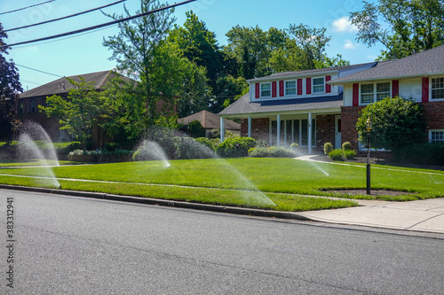 Lawn irrigation system spraying water from several nozzles onto a green grass lawn in front of a house