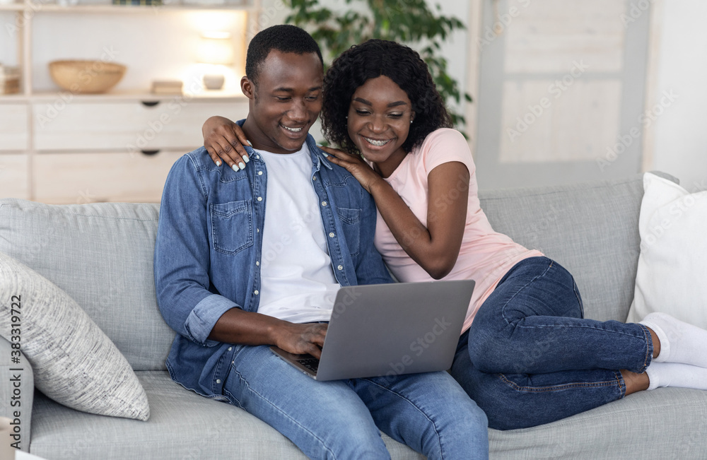 Fototapeta premium Cheerful black couple using laptop together at home
