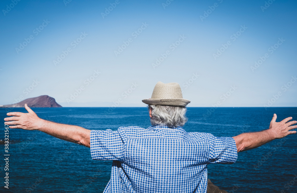 Back view of an old white haired man standing with outstretched arms in front to the sea enjoying vacation and freedom in seascape.