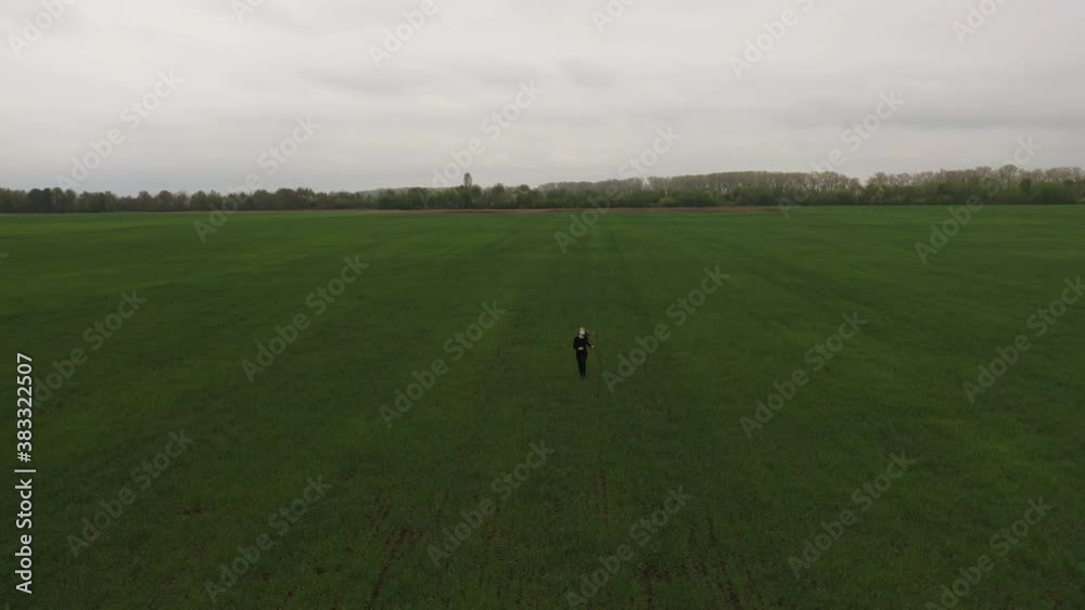 a European woman with long hair, walks run across a green field in a blue disposable protective mask from viruses, in a respirator. pandemic covid-19. Coronavirus. Drone view a European woman with long hair, walks run across a green field in a blue disposable protective mask from viruses, in a respirator. pandemic covid-19. Coronavirus. Drone view