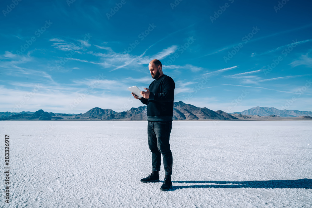 Focused male traveler using modern tablet during trip in American salt flat Focused male traveler using modern tablet during trip in American salt flat