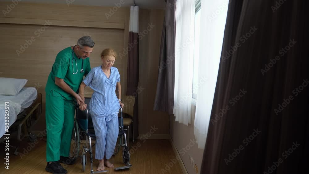 doctor helping senior woman patient trying to stand up and walking by window in hospital . Physiotherapist helping and support to Disabled old female sitting on wheelchair to physiotherapy in rehab doctor helping senior woman patient trying to stand up and walking by window in hospital . Physiotherapist helping and support to Disabled old female sitting on wheelchair to physiotherapy in rehab