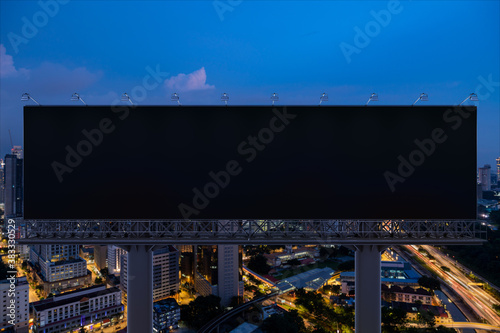 Blank black road billboard with Kuala Lumpur cityscape background at night time. Street advertising poster, mock up, 3D rendering. Front view. Concept of marketing to promote or sell idea or product.