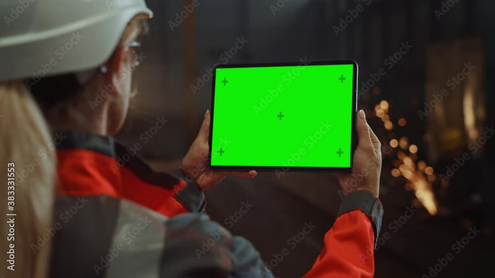 Professional Heavy Industry Engineer Uses Tablet Computer with Green Screen Mock Up Display. Female Industrial Specialist Working in a Metal Manufacture Warehouse with Sparks in the Background.