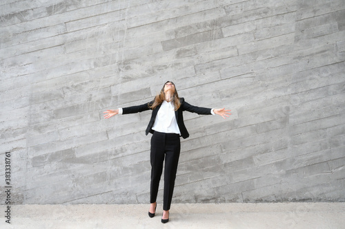 Youthful happy business woman in black suit arms wide open and raised in the air. High quality photo