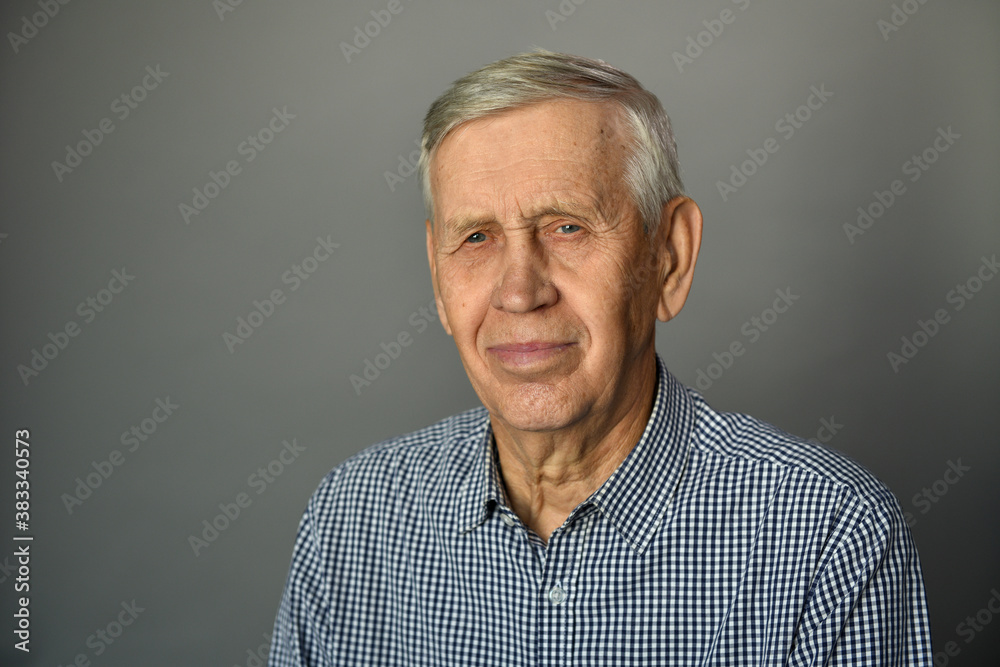 Portrait of a handsome pleased old man, 80 years old, smiling, on a gray background, studio shot.