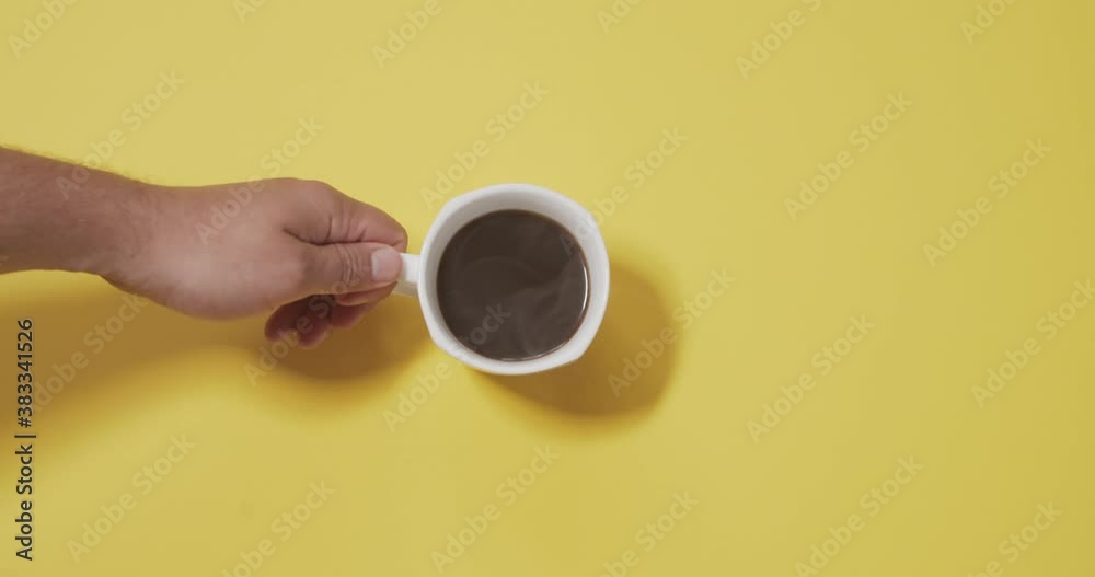 The male hand puts a cup of aromatic coffee on a yellow background in slow motion.