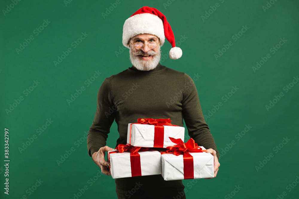 Bearded modern Santa Claus holding gifts and smiling on the green background Bearded modern Santa Claus holding gifts and smiling on the green background