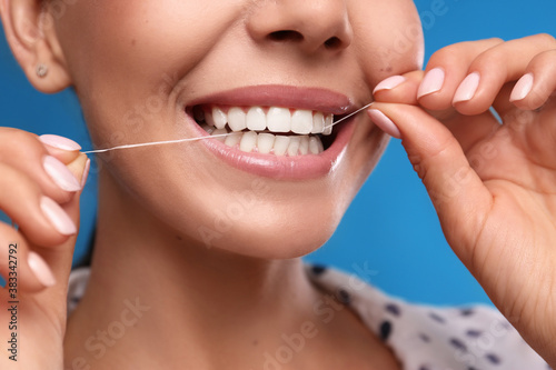 Young woman flossing her teeth on blue background  closeup. Cosmetic dentistry