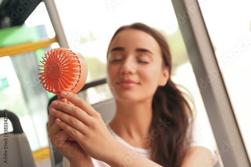 Woman with portable fan in bus, focus on hands. Summer heat