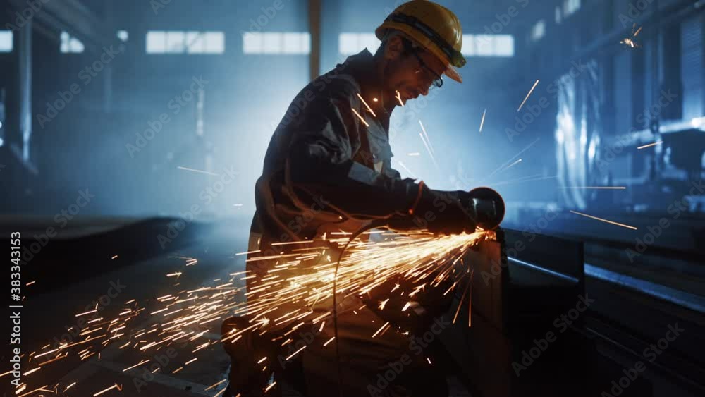 Heavy Industry Engineering Factory Interior with Industrial Worker Using Angle Grinder and Cutting a Metal Tube. Contractor in Safety Uniform and Hard Hat Manufacturing Metal Structures.