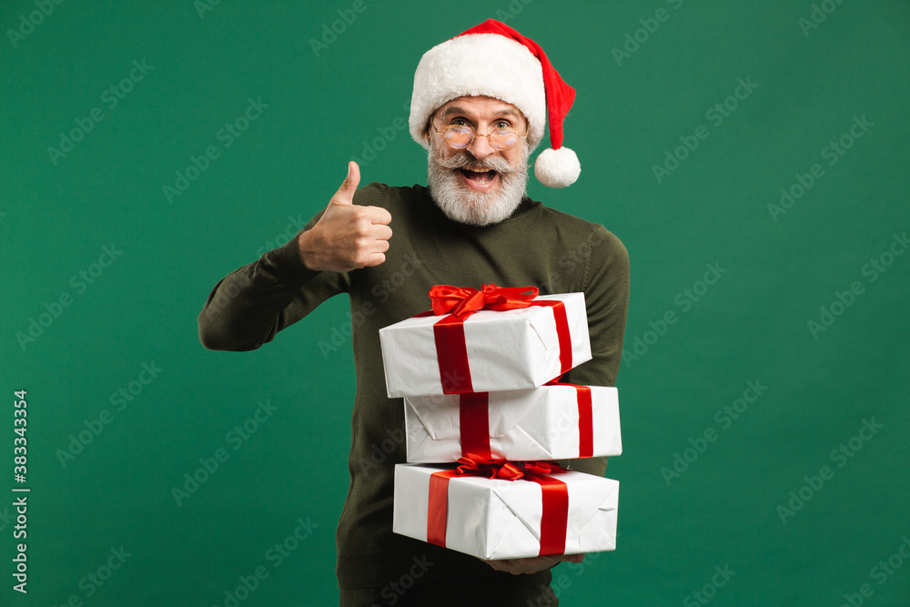 Bearded modern Santa Claus holding gifts and smiling on the green background