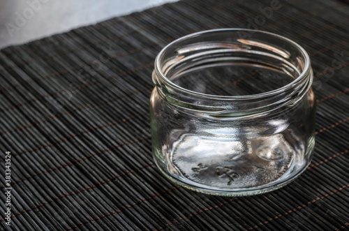 Empty glass jar on a dark bamboo napkin.