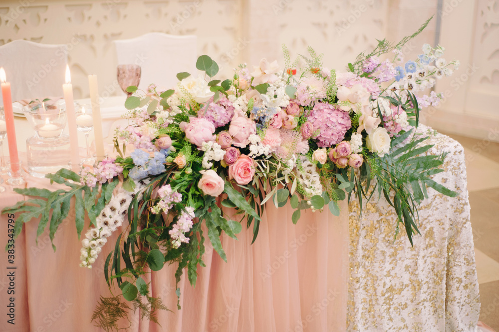 Wedding party. Newlywed's table decorated with tender pink roses, tablecloth, candles and elegant floral composition. Stylish decoration on table.