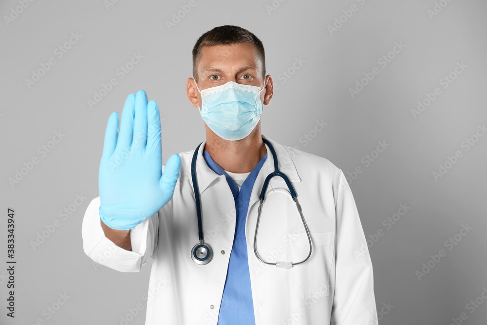 Doctor in protective mask showing stop gesture on grey background. Prevent spreading of coronavirus Doctor in protective mask showing stop gesture on grey background. Prevent spreading of coronavirus