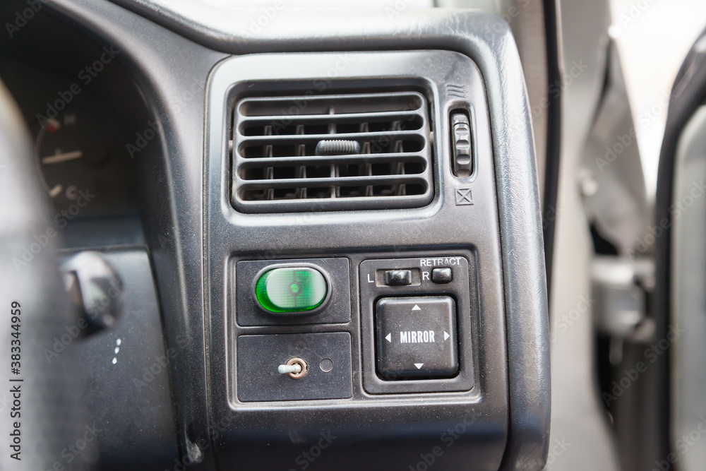 Close-up of a black plastic panel with buttons for automatically adjusting side mirrors with white markings under the air conditioning grille with air direction correction.