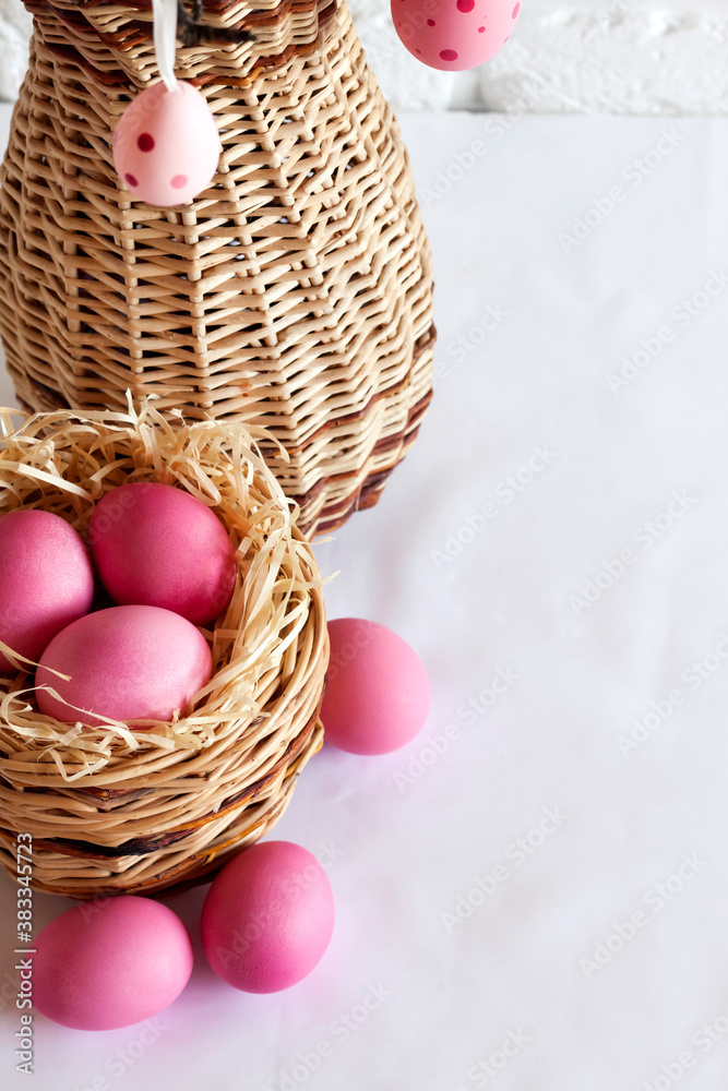 Easter composition with decorated tree branches in a wicker vase and pink colored eggs in wicker basket Easter composition with decorated tree branches in a wicker vase and pink colored eggs in wicker basket