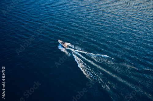 Top view of a white boat sailing to the blue sea.  Yacht in the rays of the sun on blue water.  Aerial view luxury motor boat. Drone view of a boat  the blue clear waters. © Berg
