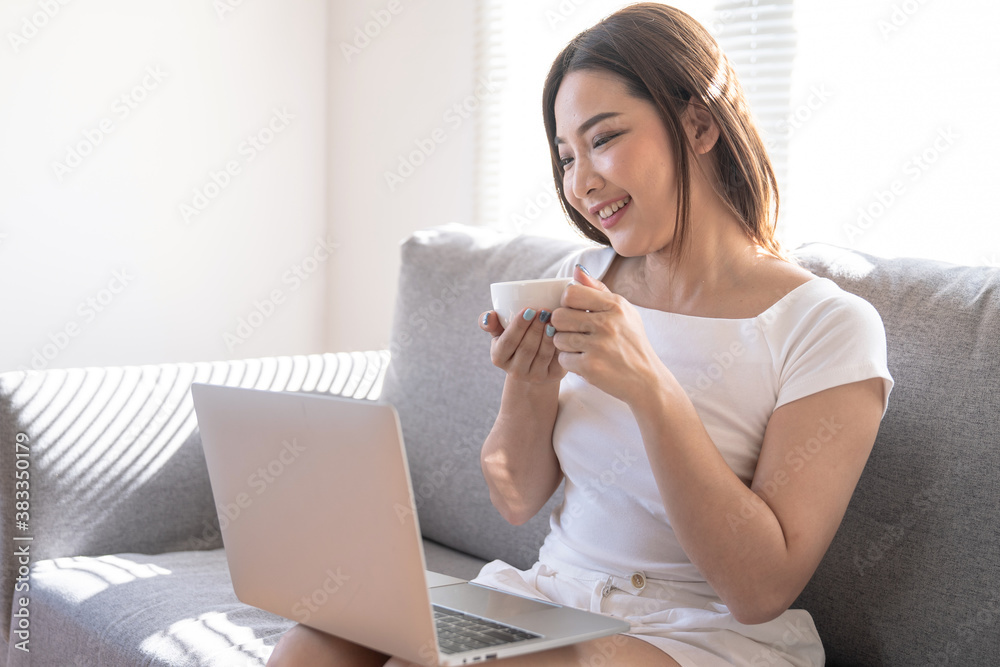 Beautiful young Asian woman working on laptop computer at the living room, Drinking coffee, Work from home. Beautiful young Asian woman working on laptop computer at the living room, Drinking coffee, Work from home.